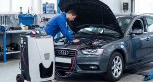 Mechanic in blue uniform inspecting an Audi car engine with diagnostic equipment in a modern workshop setting.